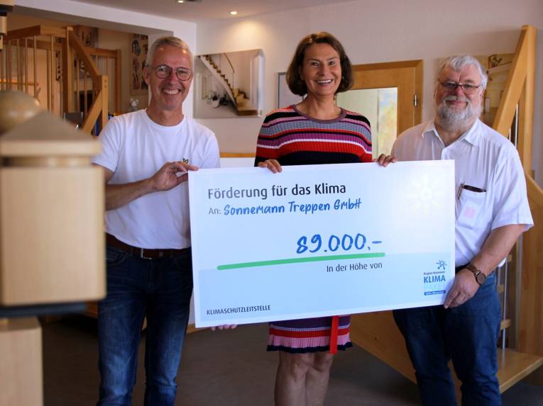 Drei Personen, die einen symbolischen Scheck über 89.000b euro in Händen halten